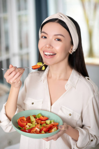 Young girl with a hair bandage eating a vegetarian salad. - Фото, изображение