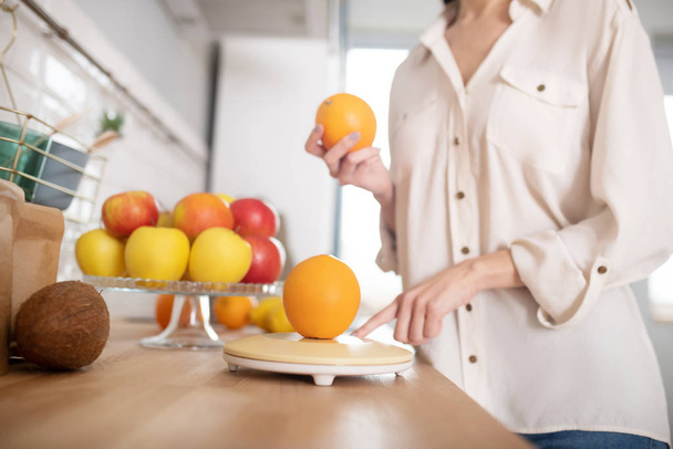 Woman in beige blouse standing near table with fruits. - Fotoğraf, Görsel