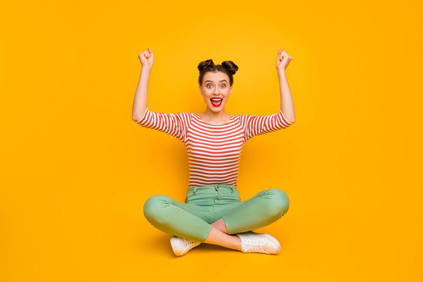 Hooray Full body photo of pretty crazy excited lady sit floor legs crossed raise fists wear striped red white shirt green pants footwear isolated yellow color background - Zdjęcie, obraz