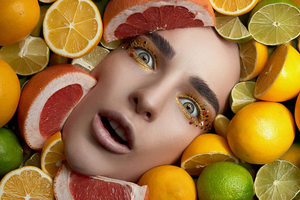 Parlak bir fotoğrafta parlak makyajlı güzel bir model meyve, limon ve limon narencisinin arka planında ağzı açık yatıyor. Üst Uç rötuş - Fotoğraf, Görsel