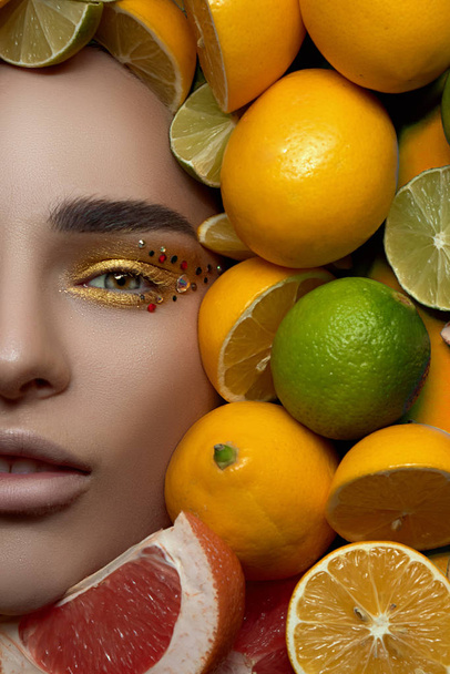 beautiful fashion professional model with bright makeup on a bright photo is lying with his mouth open on a background of fruit, lemon and lime citrus. High End retouch. Close up portrait - Fotografie, Obrázek