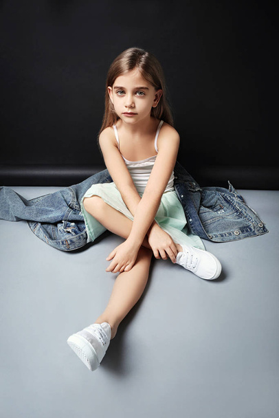 Cute fashionable girl sitting near dark background - Фото, изображение