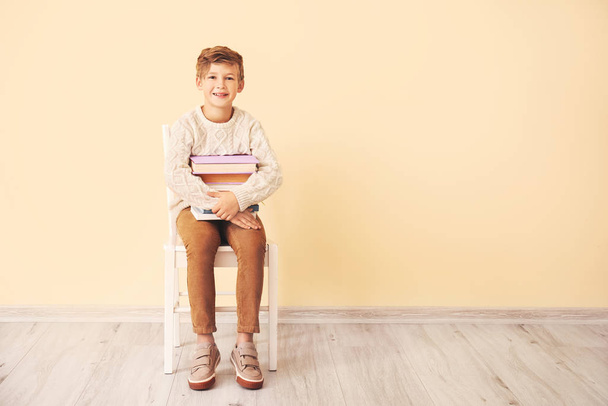 Μικρό αγόρι με τα βιβλία κάθεται κοντά στον τοίχο χρώμα - Φωτογραφία, εικόνα