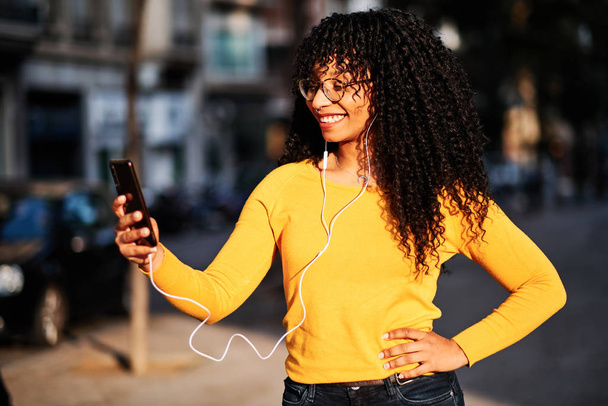 une jeune afro-américaine aux cheveux bouclés écoutant de la musique avec mobile - concept lifestyle
 - Photo, image
