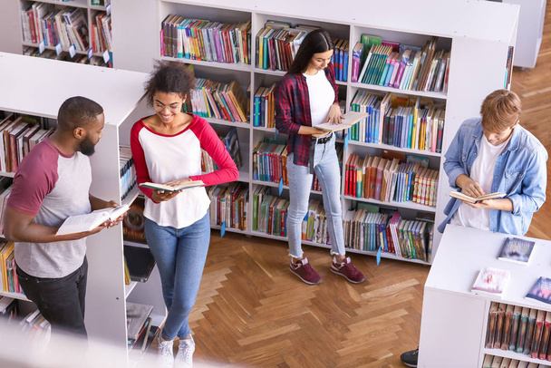 Jóvenes estudiantes leyendo libros mientras se preparan para el examen en la biblioteca
 - Foto, imagen