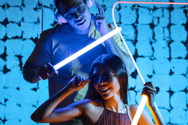 Portrait tonique de jeune couple avec des lampes au néon sur fond de couleur sombre
 - Photo, image