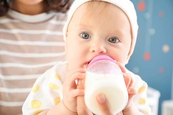Мать кормит ребенка молоком из бутылки дома, крупным планом
 - Фото, изображение