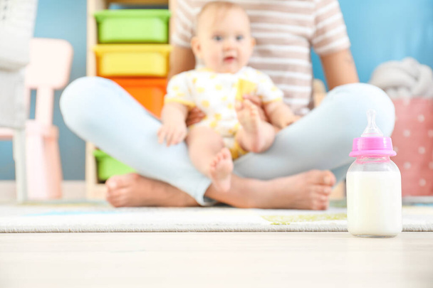 Mother with little baby and bottle of milk on floor - Фото, зображення