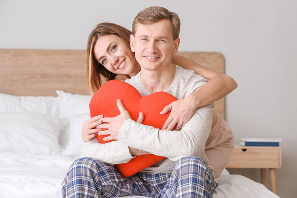 Красивая пара с красным сердцем на кровати дома
 - Фото, изображение