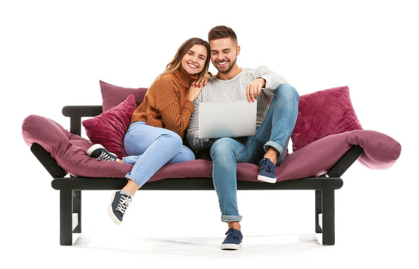 Young couple with laptop sitting on sofa against white background - Valokuva, kuva