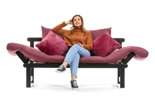 Young woman listening to music while sitting on sofa against white background - Photo, Image
