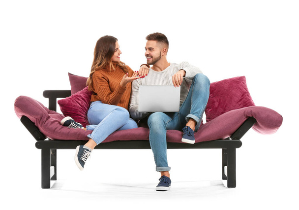 Junges Paar mit Laptop sitzt auf Sofa vor weißem Hintergrund - Foto, Bild