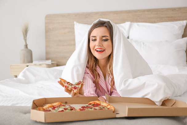 Morgen der schönen jungen Frau, die leckere Pizza im Schlafzimmer isst - Foto, Bild