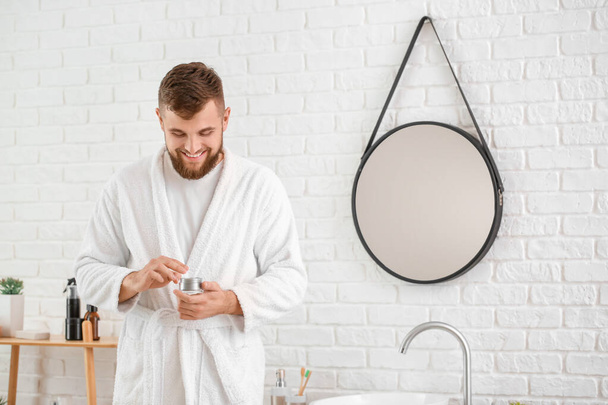 Handsome young man with jar of cream in bathroom - Photo, Image