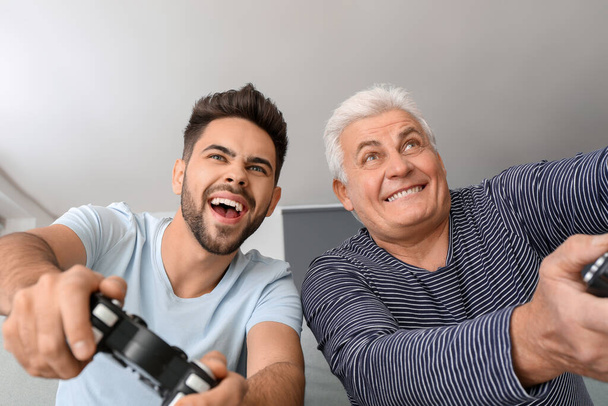 Młody człowiek i jego ojciec grają w gry wideo w domu - Zdjęcie, obraz