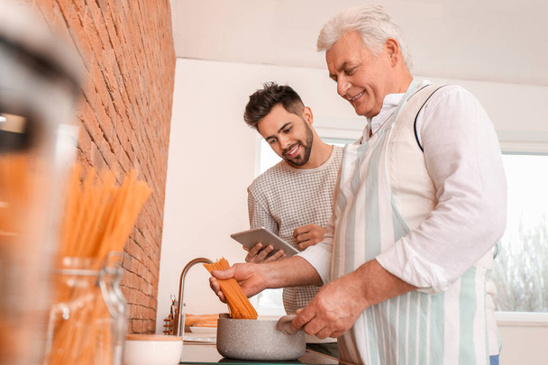 Young man and his father cooking in kitchen - Photo, image