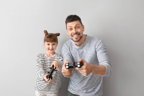 Vater und seine kleine Tochter spielen Videospiele auf grauem Hintergrund - Foto, Bild