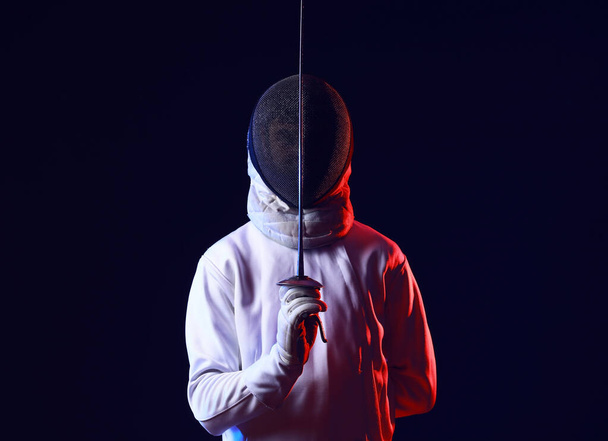 Toned photo of young fencer on dark background - Фото, изображение