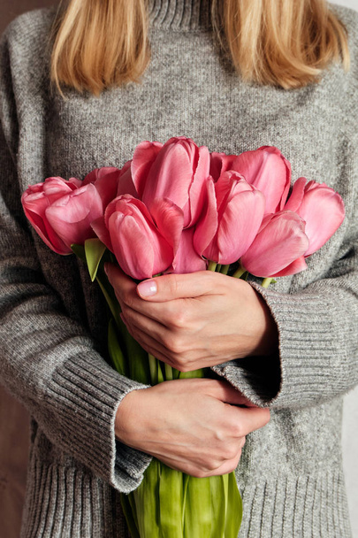 Happy woman holds tulips in her hands. Florist girl gathered a bouquet. Beautiful pink flowers. Blossom petal. Gift for the holiday celebration, springtime mood. Romantic surprise from a loved one - Photo, Image