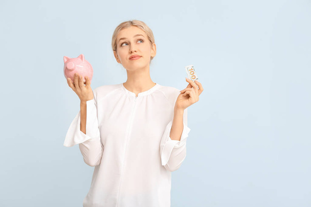 Thoughtful young woman with piggy bank on color background - Photo, Image