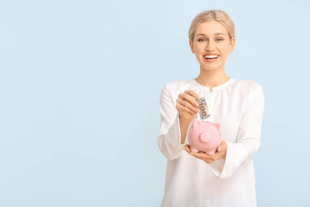 Young woman with piggy bank on color background - Фото, изображение
