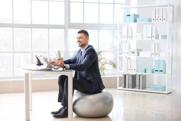 Empresário sentado na bola de fitness enquanto trabalhava no escritório
 - Foto, Imagem