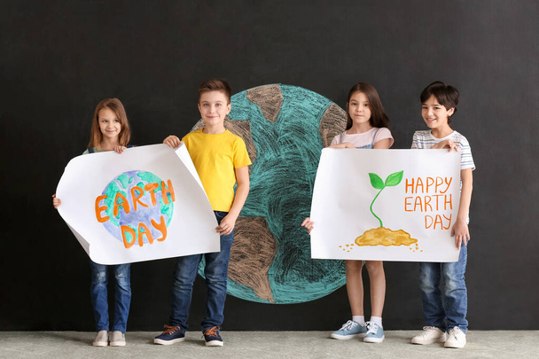 Little children with posters and drawing of planet on dark background. Earth Day celebration - Fotografie, Obrázek