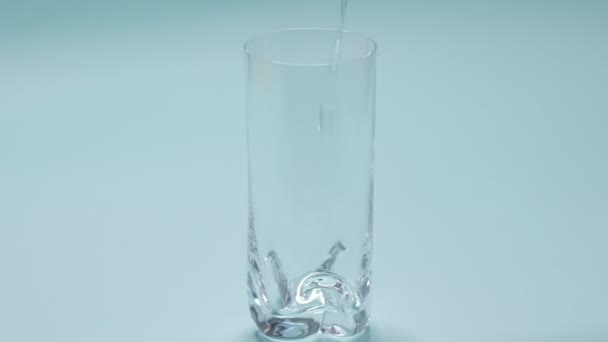 studio shoot of water pouring into transparent glass on blue background. Slow Motion video. Close up top view - Záběry, video