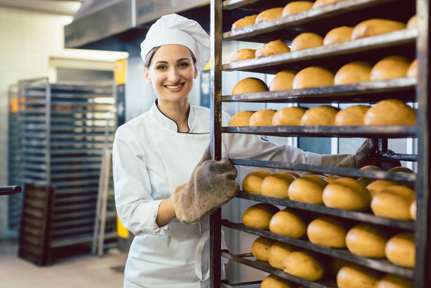 Pekař válí tácy s čerstvým chlebem přes pekárnu - Fotografie, Obrázek