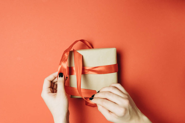 Partial view of woman tying ribbon on gift box isolated on red - Photo, Image