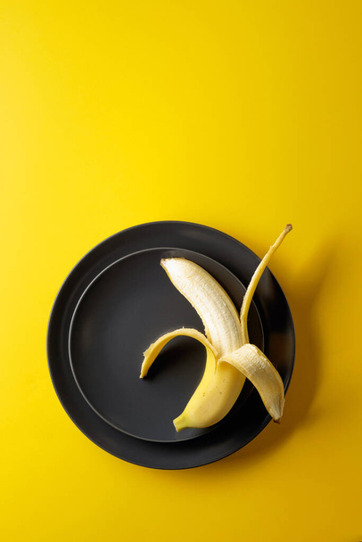 Zralý šťavnatý banán na černém talíři.  - Fotografie, Obrázek