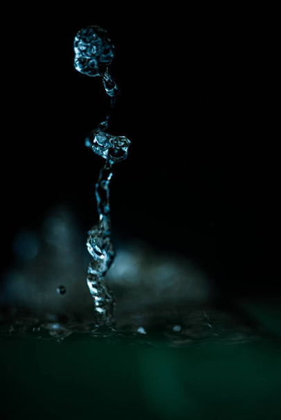 A vertical  closeup shot of a blue water splash in motion on a black background - Фото, изображение