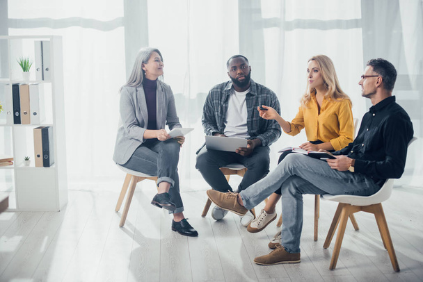Multikulturelle Kollegen mit Gadgets sitzen und reden im Büro  - Foto, Bild