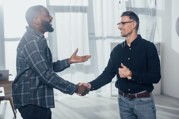 smiling multicultural colleagues shaking hand and showing like  - Photo, Image