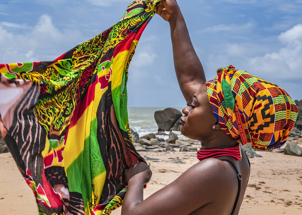 Africa Ghana woman on the beautiful beach of Axim, located in Ghana West Africa. Headdress in traditional colors from Africa. - Photo, Image