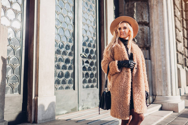 Spring fashionable female accessories. Stylish woman walking in teddy coat hat and holding handbag outdoors. Clothes - Photo, Image