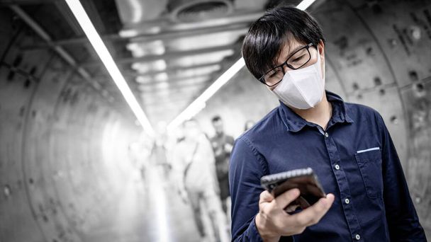 aziatische man dragen masker met behulp van telefoon in metro - Foto, afbeelding