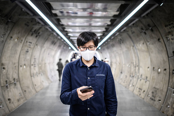 Hombre asiático usando máscara usando el teléfono en el metro
 - Foto, Imagen