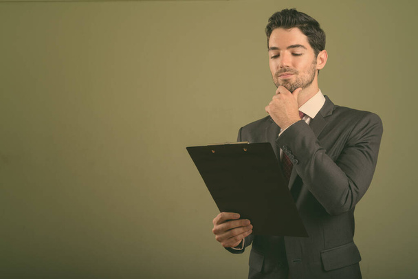 Jonge knappe zakenman draagt pak tegen gekleurde achtergrond - Foto, afbeelding