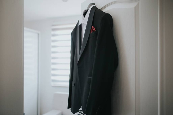 A black suit and a white shirt is hanging from hanger from the door - Photo, image