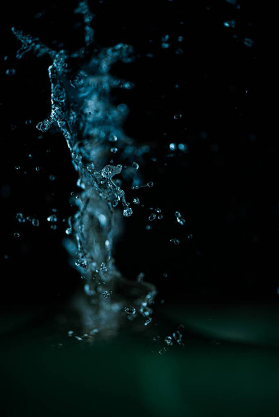 A vertical closeup shot of a blue water splash in motion on a black background - Foto, Bild