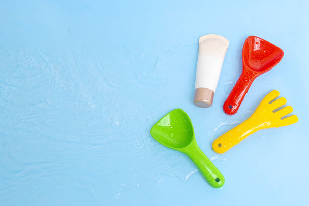 Sonnencreme SPF-Lotion, um Kinderhaut von der Sonne mit bunten Wasserspielzeug auf blauer Wasseroberfläche des Pools, Draufsicht zu beheben. Konzept UV-Schutzprodukt, Sommer-Kinderkosmetik. - Foto, Bild