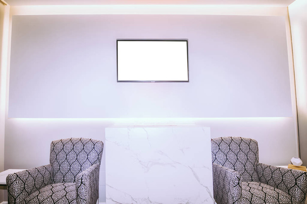Moderní čekárna se dvěma křesly a velkým bílým plakátem ve zdi, který obsahuje prázdnou televizní obrazovku. - Fotografie, Obrázek