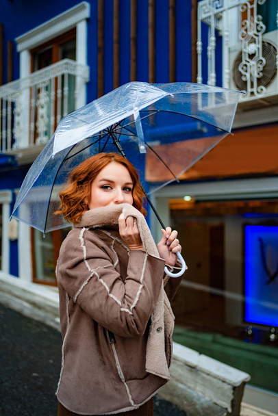 red-haired girl brown clothes under umbrella  - Foto, afbeelding