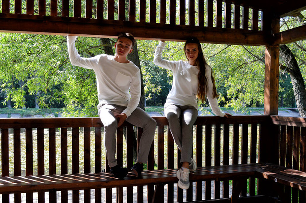 Молодая девушка и молодой человек в одной одежде сидят на деревянной скамейке
. - Фото, изображение