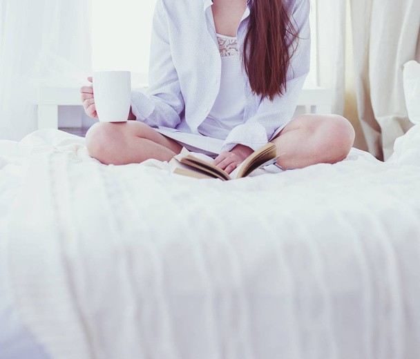 Woman sitting in bed reading a book and having breakfast - Fotografie, Obrázek