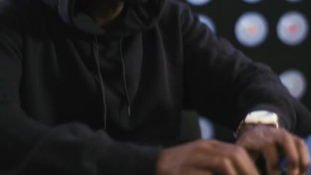 Endişeli görünümlü Afro-Amerikalı yetişkin bilgisayar korsanı siyah kapüşonlu bilgisayar odasında oturuyor ve aktif olarak klavyeye bir şey yazıyor, karanlık odada görüntüye bakıyor.. - Video, Çekim