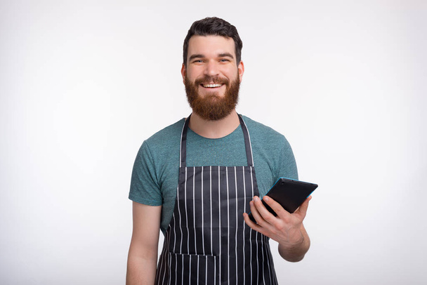 Schöner bärtiger Koch mit Schürze hält sein Tablet in der Hand - Foto, Bild