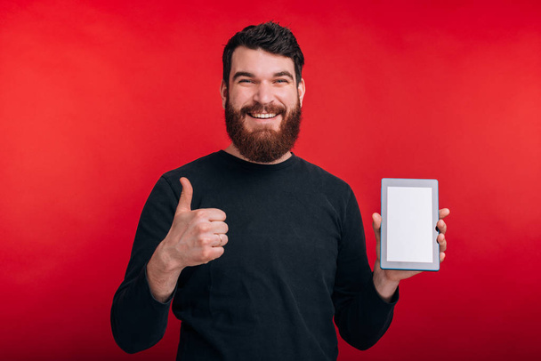 Sonriente hombre está mostrando el pulgar hacia arriba y la pantalla en blanco de una tableta en
  - Foto, Imagen