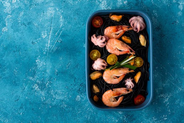 spaghettis noirs végétariens avec crevettes royales, moules, poulpes et légumes en assiette bleue sur fond bleu
 - Photo, image